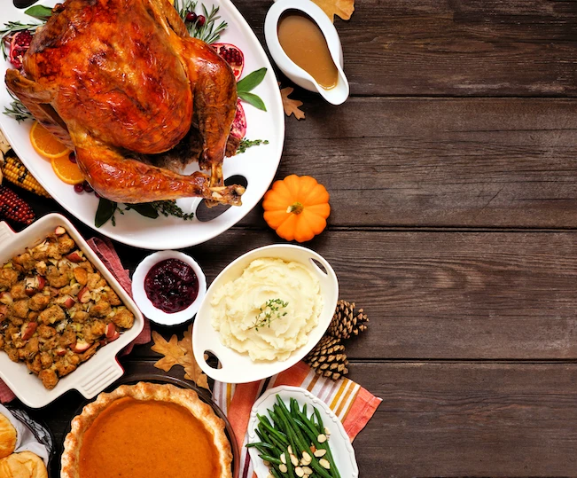 Thanksgiving table with traditional dishes like turkey, stuffing, cranberry, potatoes, pumpkin pie, and gravy